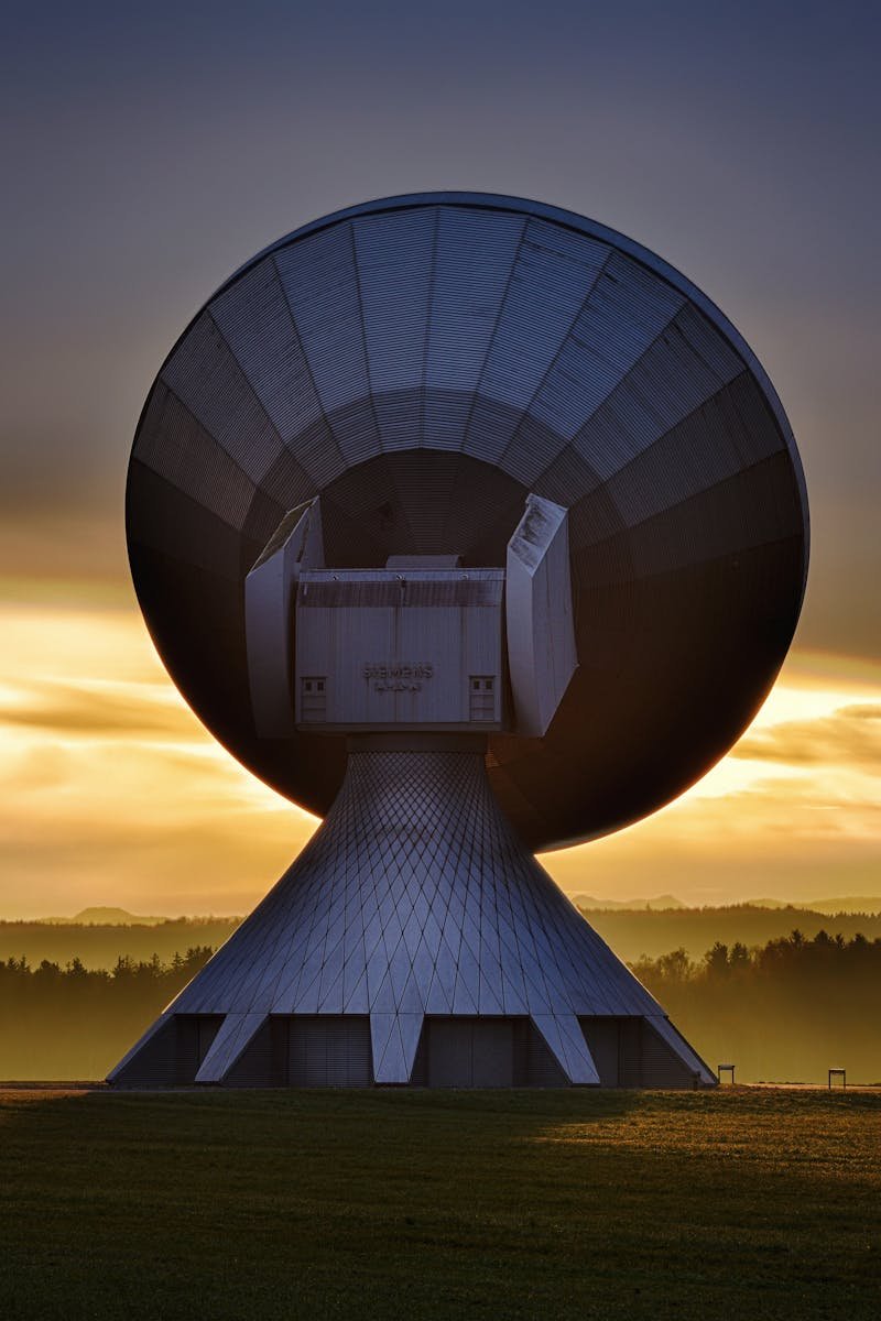 Large satellite dish silhouette against a colorful sunset, showcasing broadcasting technology.