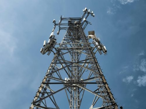 A low-angle shot of a tall metal communications tower with multiple antennas against a clear blue sky.